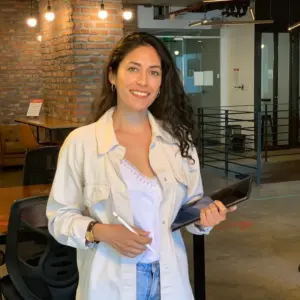 Makarena Díaz De pie sosteniendo un iPad con una chaqueta y camiseta blanca