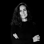 Marta posando frente a la cámara en primer plano sonriendo con los brazos cruzados delante con jersey negro y fondo negro