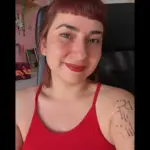 Sara Guajardo sentada en una silla negra sonriendo a la camara con una camiseta roja y los labios pintados de rojo